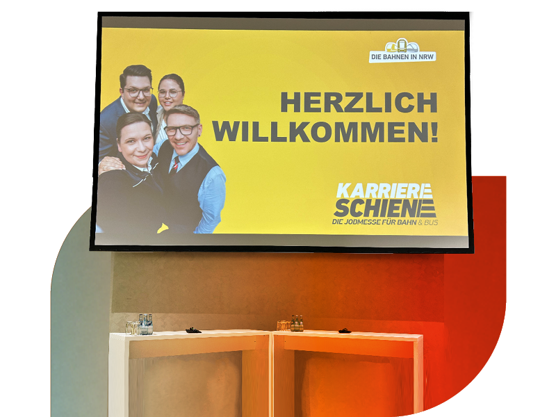 Bildschirm mit der Aufschrift „Herzlich willkommen! Karriereschiene“ und Porträts mehrerer Personen.