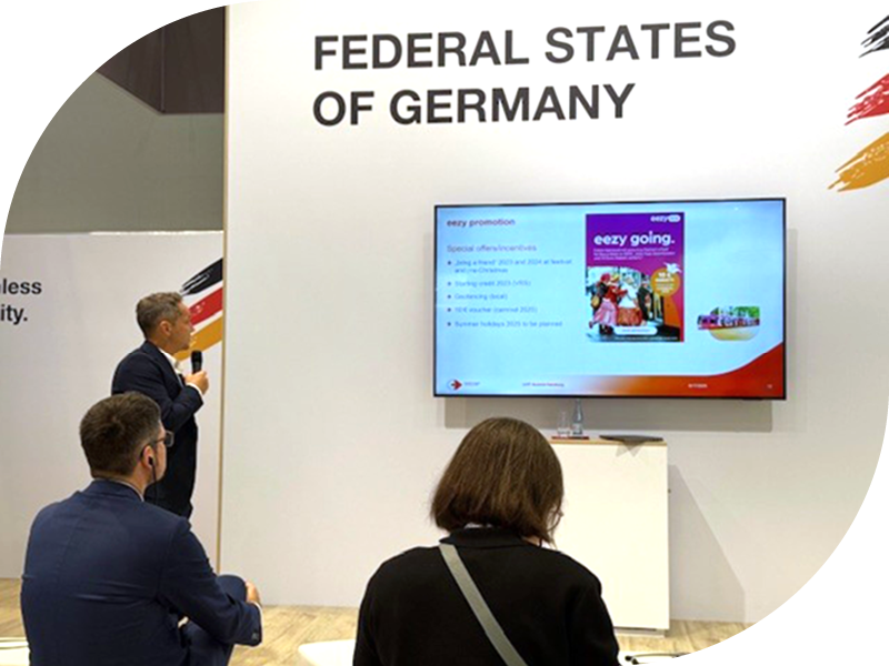 Besucherinnen und Besucher verfolgen eine Präsentation am Messestand „Federal States of Germany“.