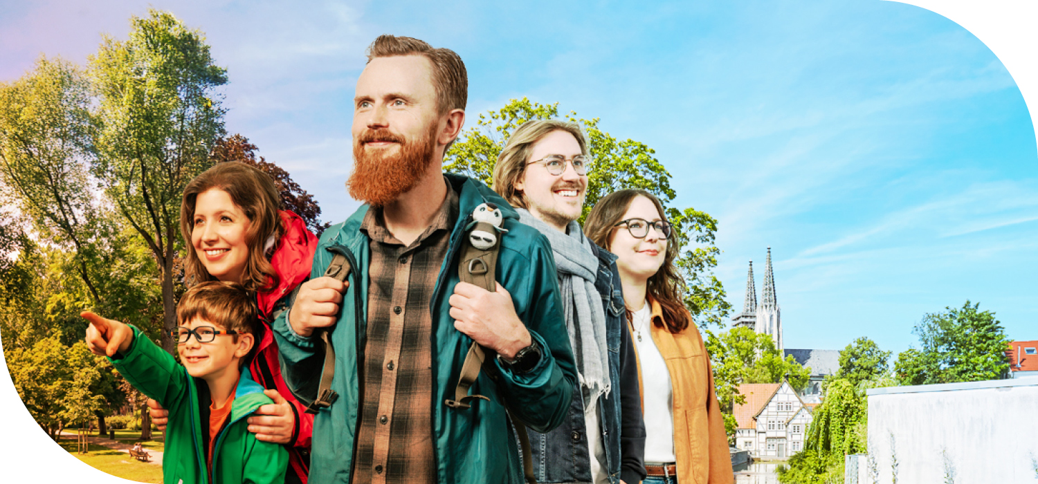 Gruppe von Wandernden mit Rucksäcken vor einer grünen Stadtkulisse mit dem Kölner Dom im Hintergrund.