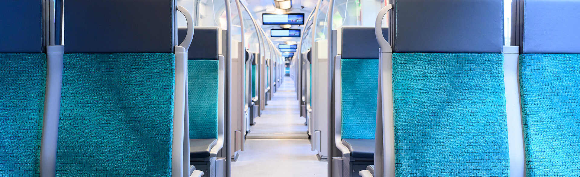 Innenraum eines öffentlichen Verkehrsmittels mit blauen Sitzen und Haltestangen.