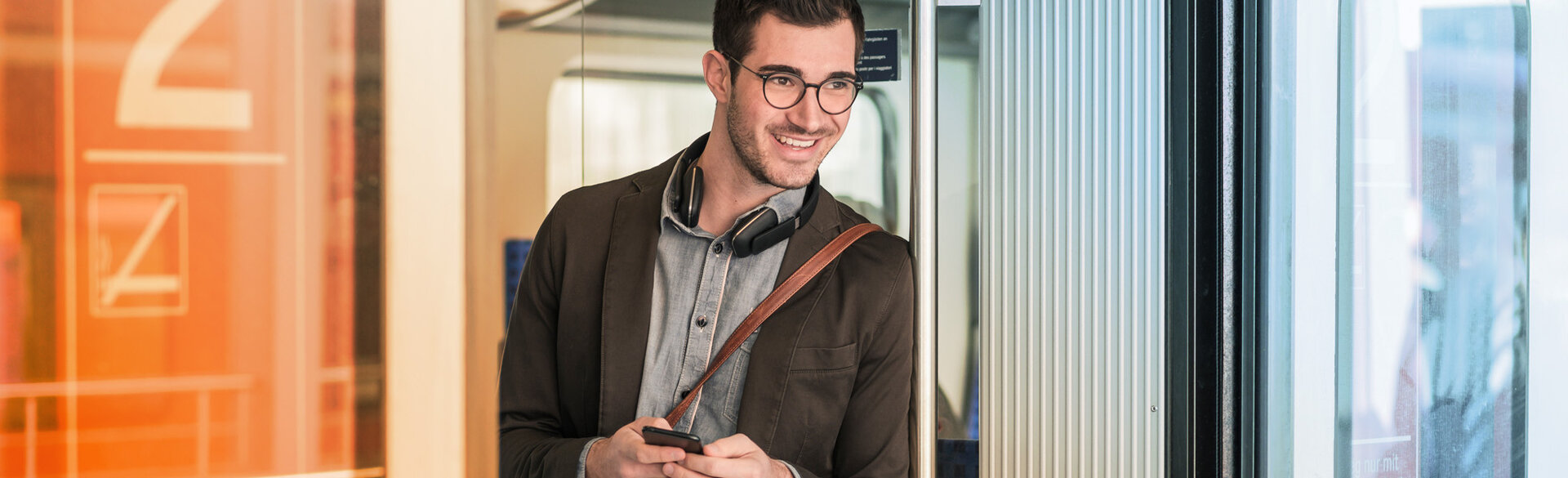 Mann mit Brille steht in einem modernen Innenraum und blickt in die Kamera.