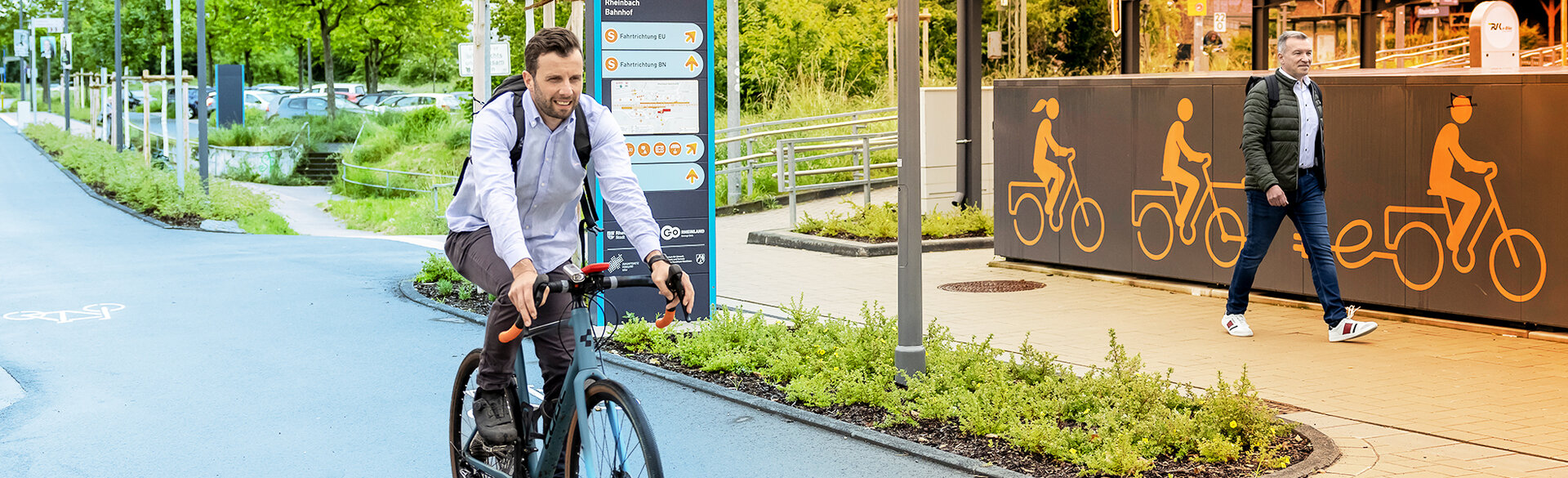 Ein Radfahrer und ein Fußgänger sind an einem Bahnhof unterwegs. Im Hintergrund weisen orangefarbene Piktogramme auf verschiedene Formen der Fahrradmobilität hin.