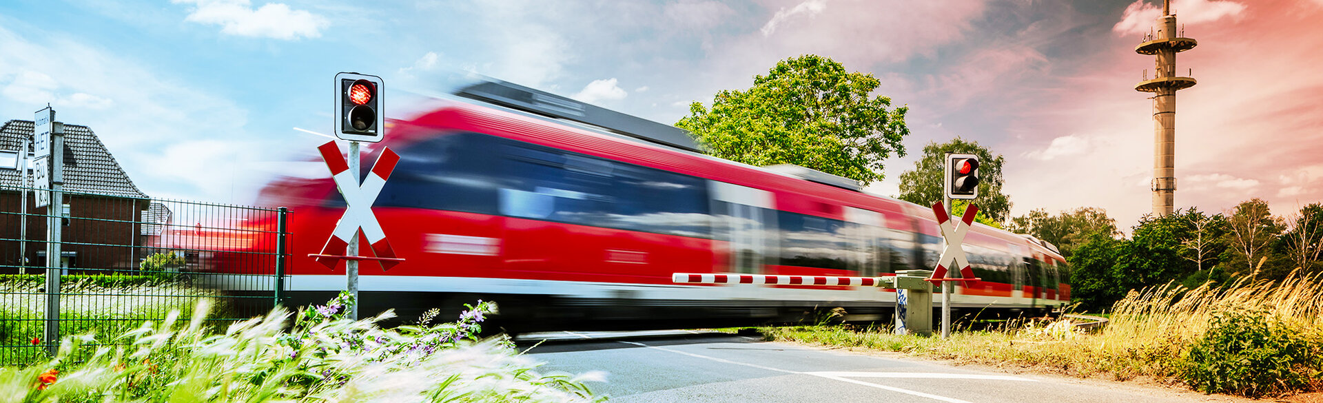 Roter Regionalzug fährt auf einer Bahnstrecke durch eine ländliche Umgebung.
