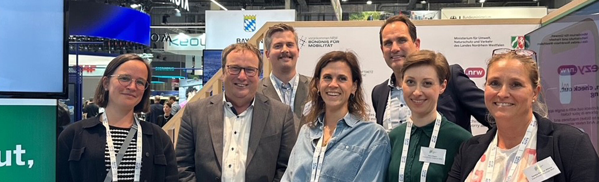 Gruppe von Besucherinnen und Besuchern auf einer Messe, die gemeinsam in die Kamera lächelt.