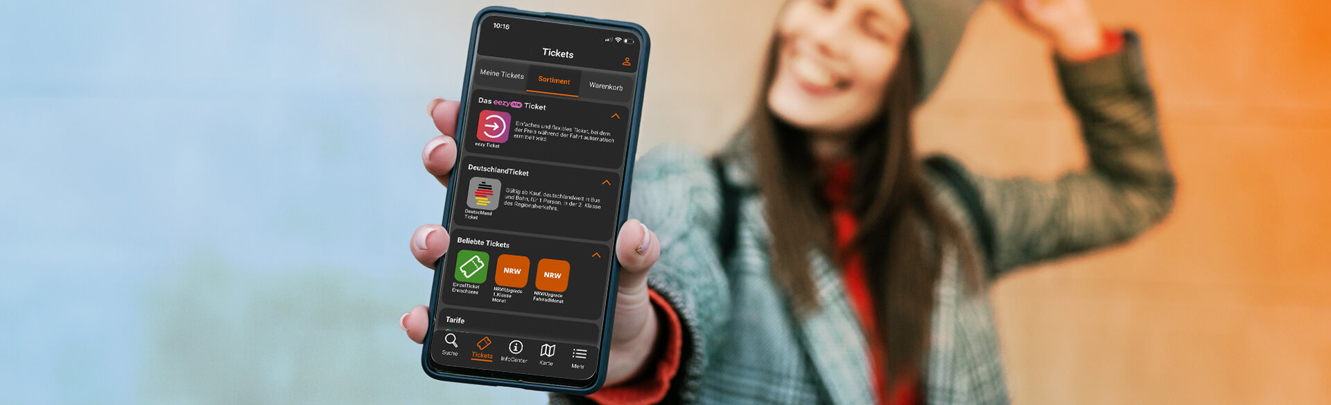 Eine Person hält ein Smartphone mit geöffneter mobil.nrw-App in die Kamera. Auf dem Display ist die Ticketübersicht mit eezy-Ticket, Deutschlandticket und weiteren Ticketangeboten zu sehen.