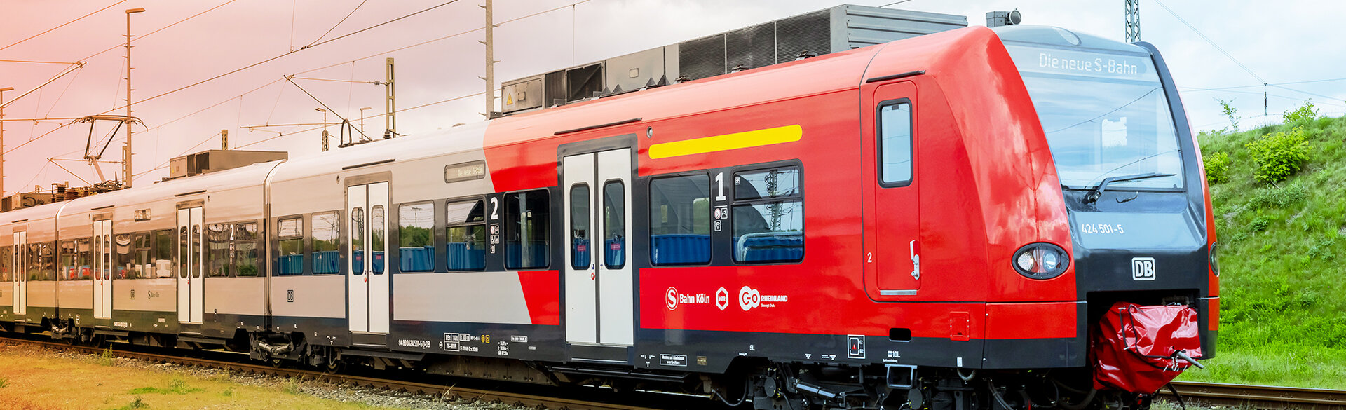 Roter Regionalzug fährt auf einer Bahnstrecke durch eine grüne Landschaft.
